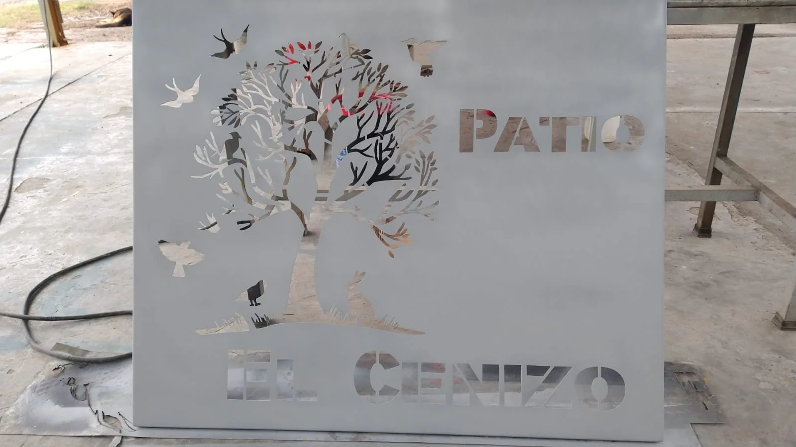 Letrero Patio El Cenizo cortado en placa de acero, con árbol y pájaros